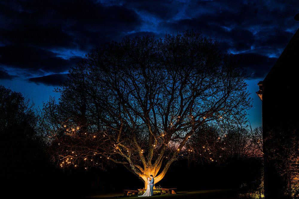 Couple embraces under illuminated tree at night.