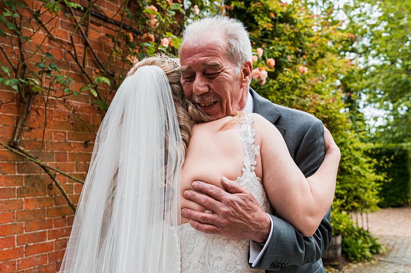 Bride hugs elderly man at garden wedding.