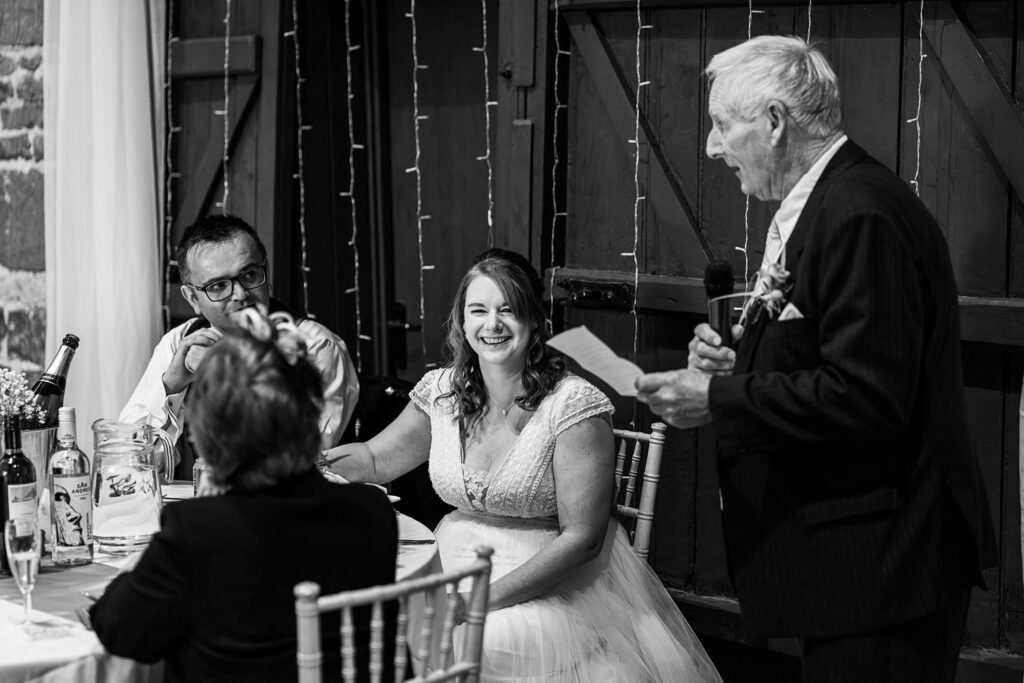 Elderly man giving wedding speech to smiling bride.