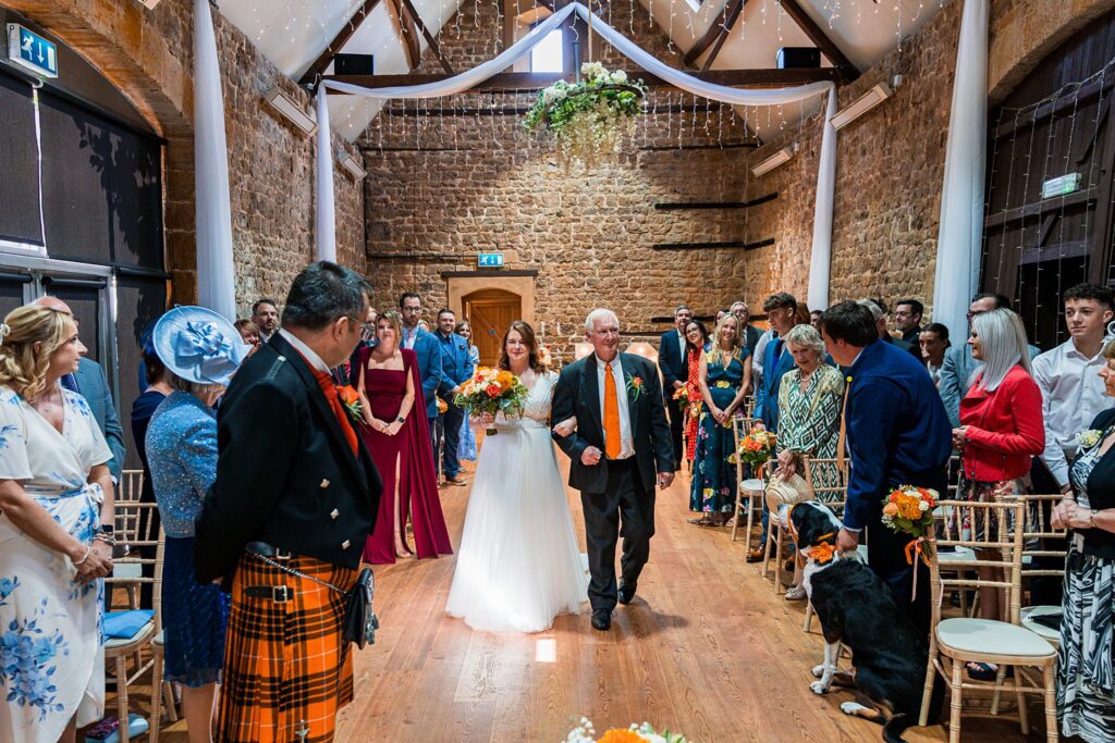 Bride and father walking down wedding aisle indoors.