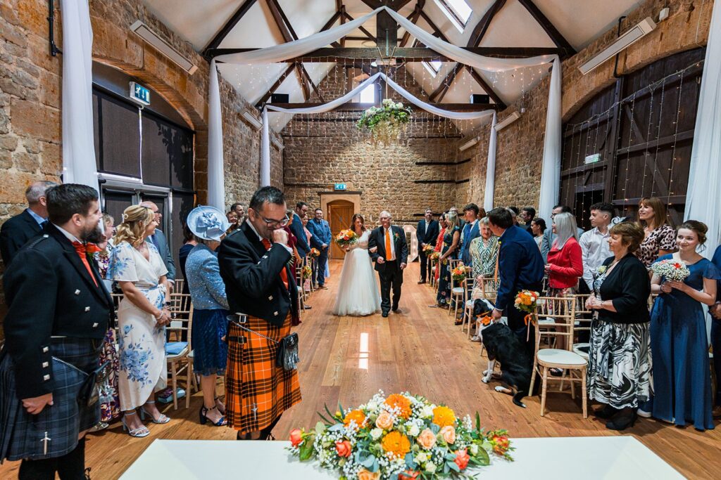 Bride walks down aisle with father, guests watching.