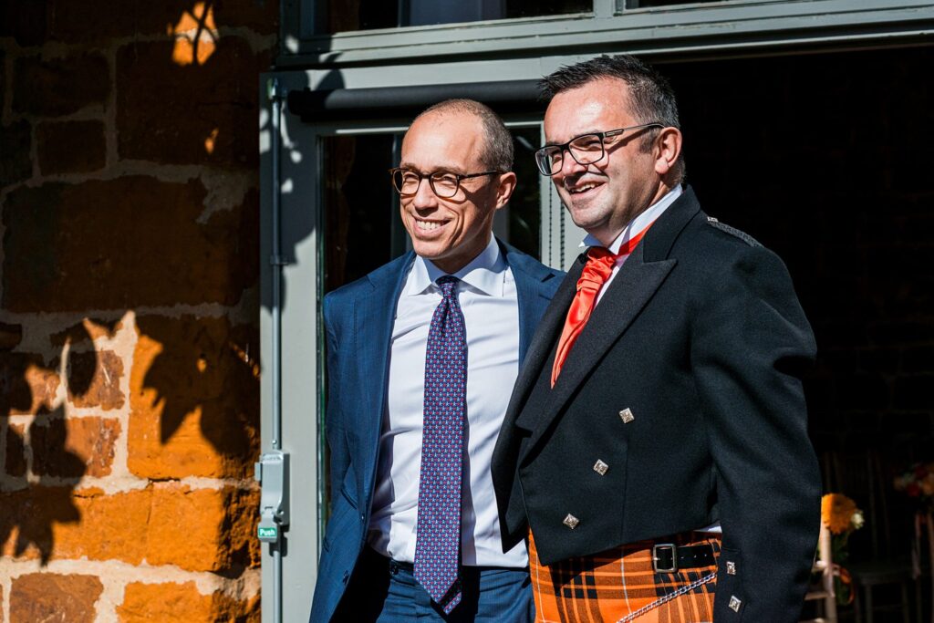 Two men in suits and kilt outside building.