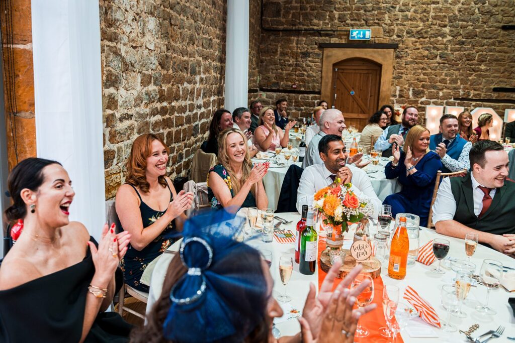 Wedding guests laughing and clapping at reception table.