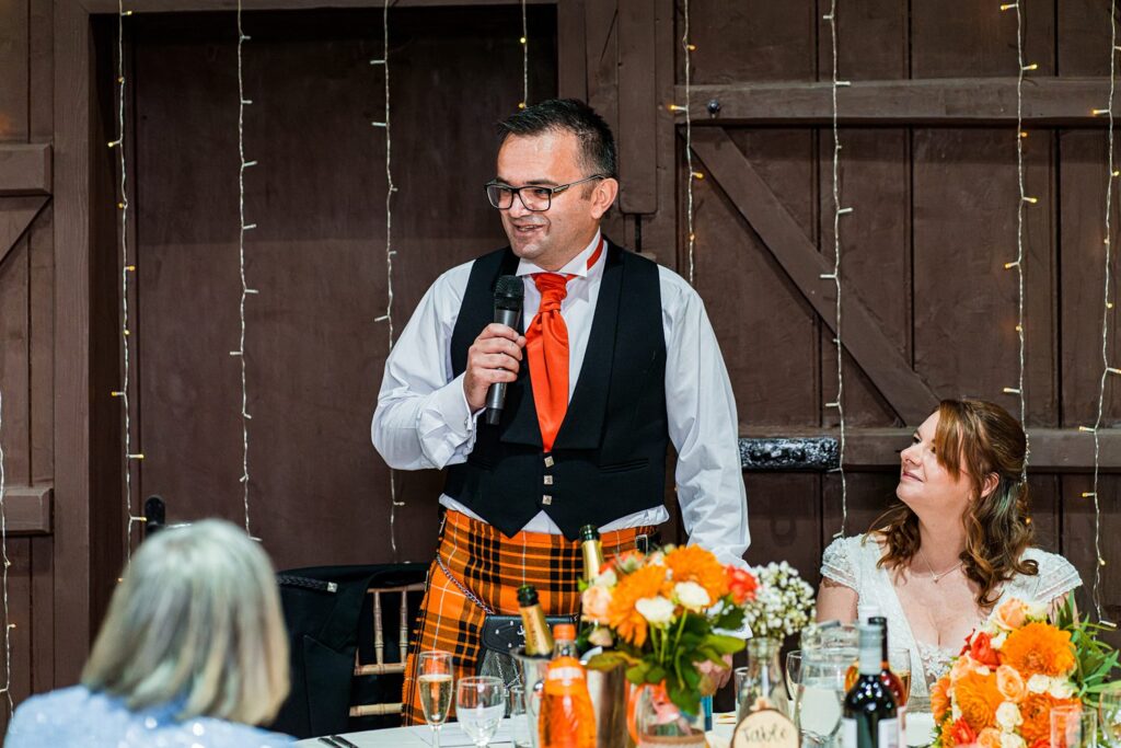 Wedding speech by kilted man with orange tie.