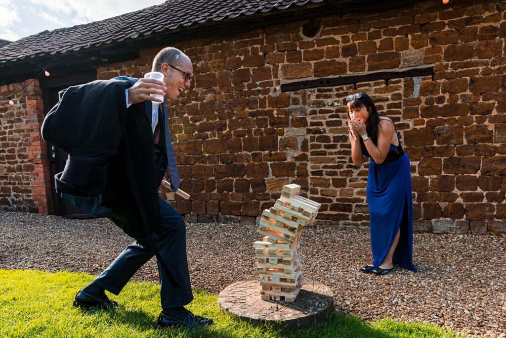 Man knocks over outdoor Jenga tower, woman surprised.