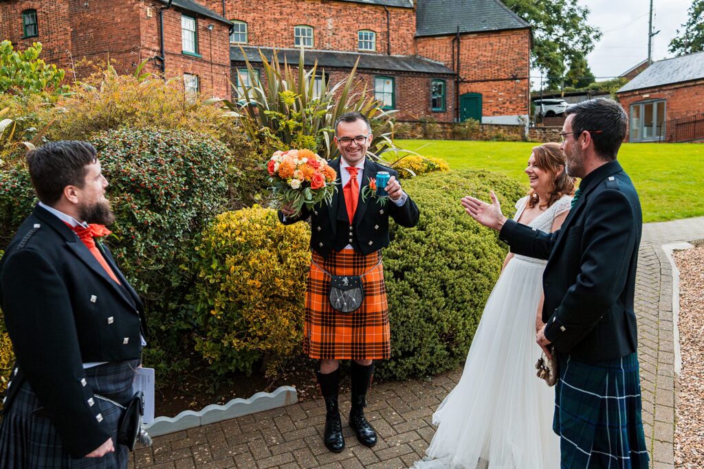 Smiling man in kilt holding flowers and drink.
