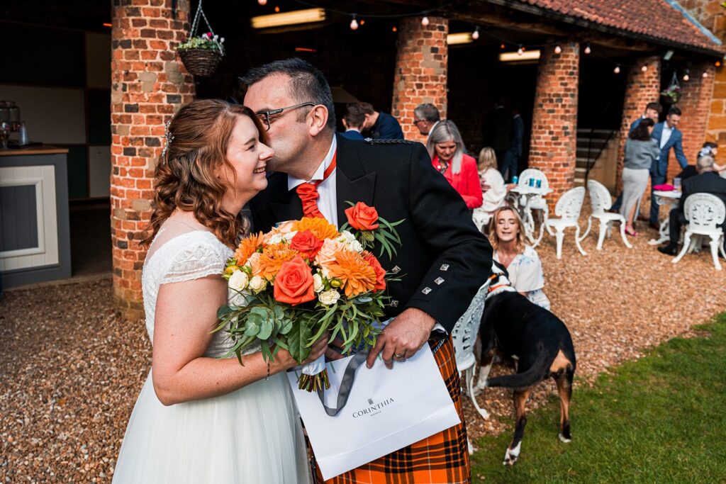 Couple embraces with vibrant floral bouquet, outdoor event.
