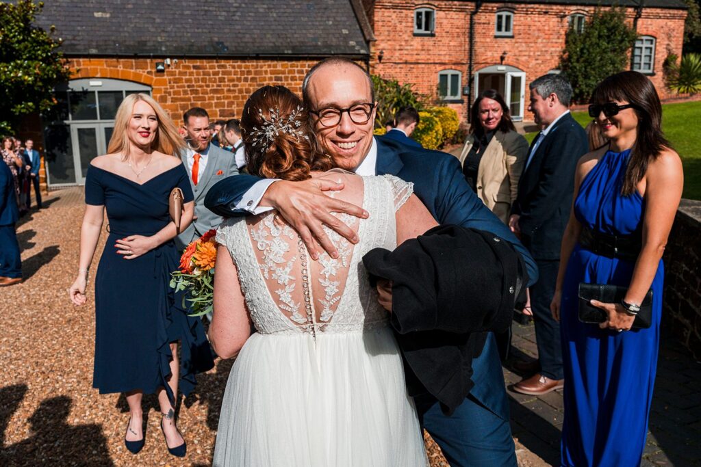 Wedding guests smiling and hugging outside venue.