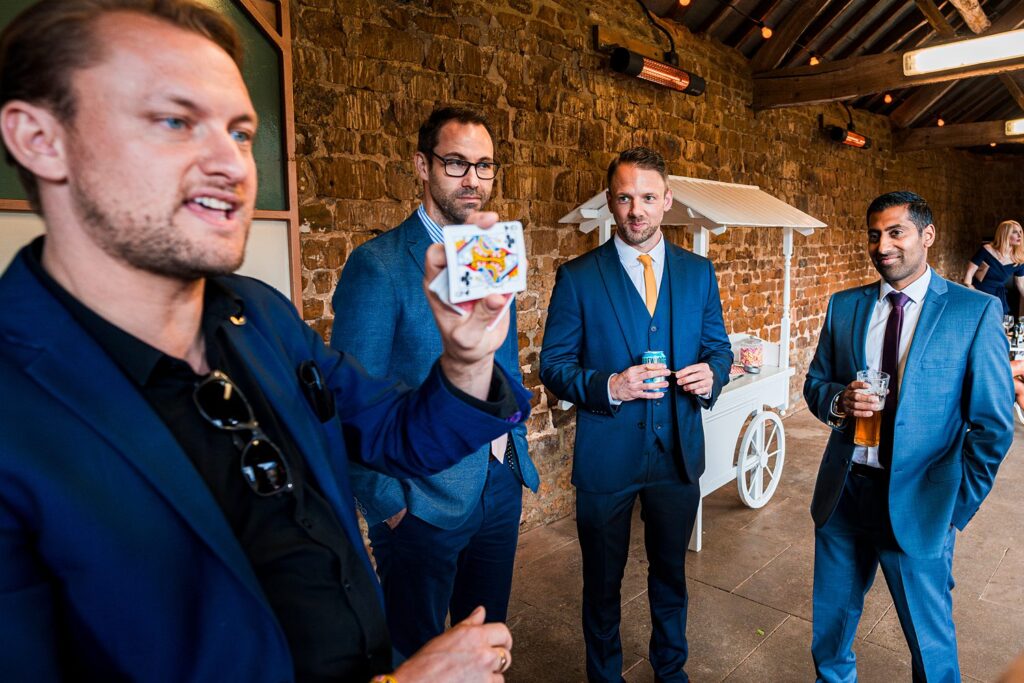 Magician performs card trick for three men indoors.
