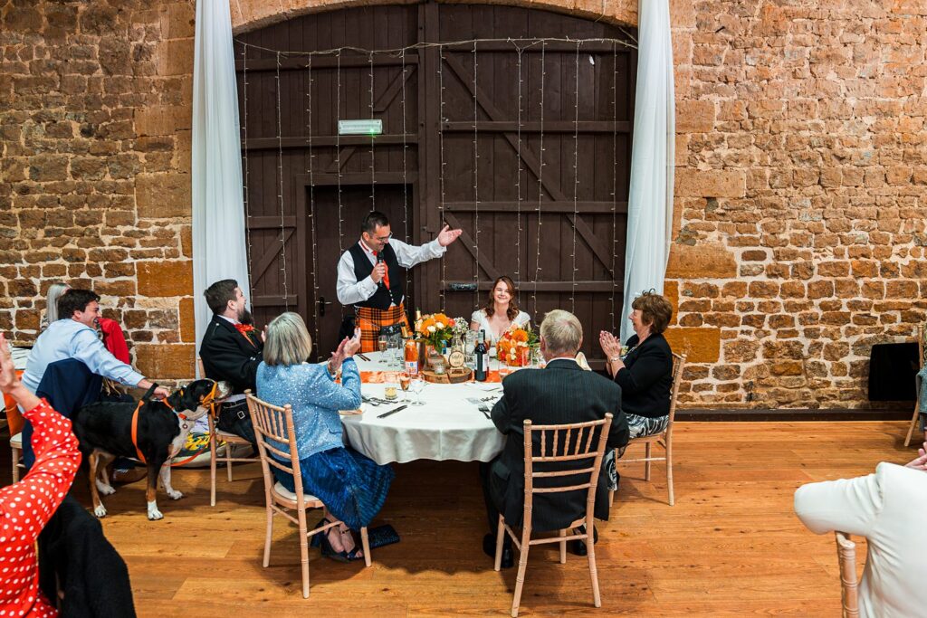 Wedding speech at rustic reception with guests applauding.