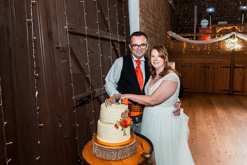 Couple cutting wedding cake at rustic venue.