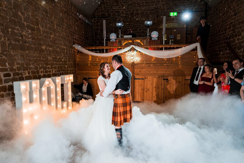 Bride and groom dancing amid wedding smoke.