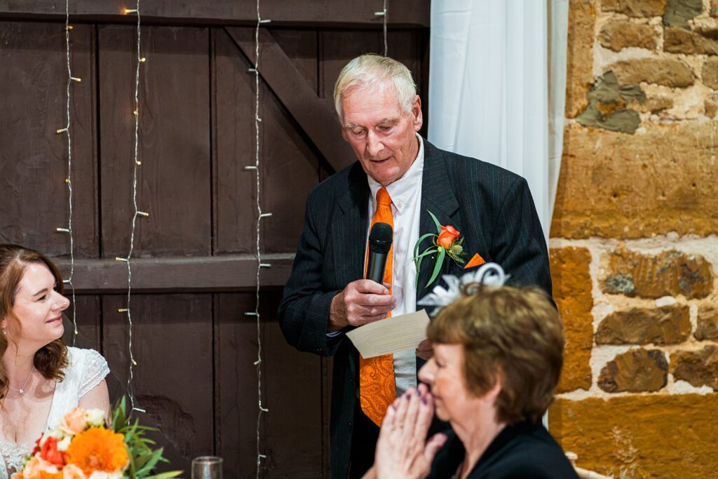 Older man giving wedding speech, holding microphone.