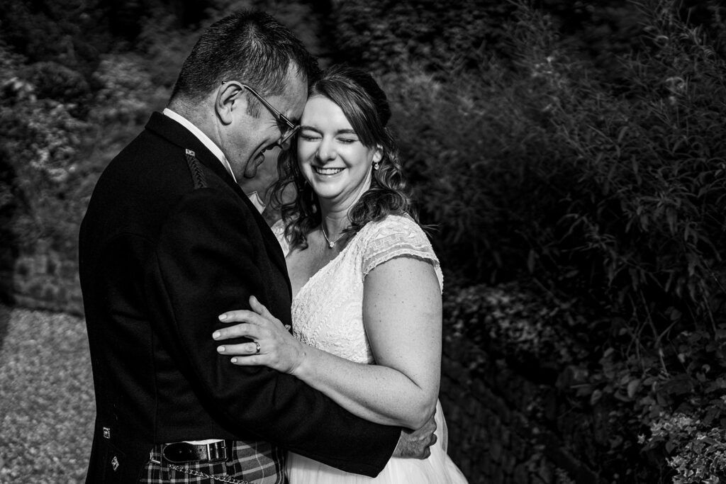Smiling couple embraces outdoors in wedding attire.