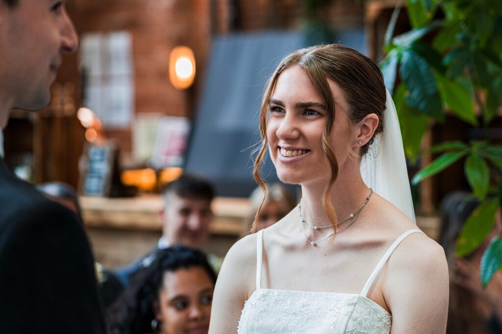 Bride smiling during wedding ceremony indoors.