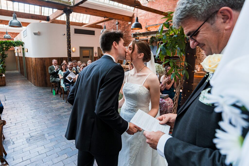 Bride and groom kissing at indoor wedding ceremony.