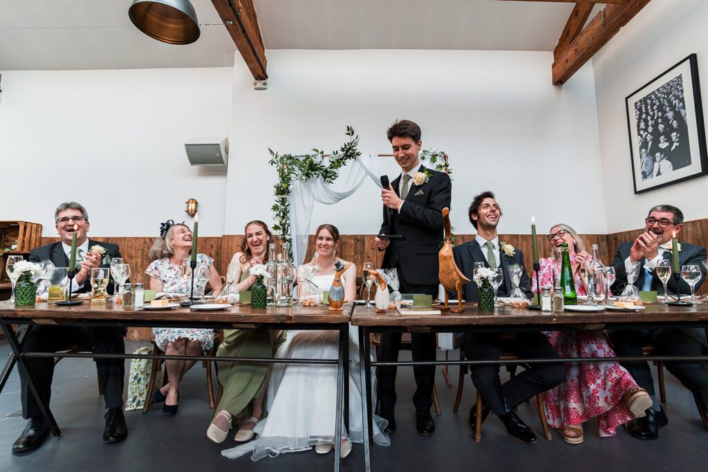Wedding party laughing during speech at reception.