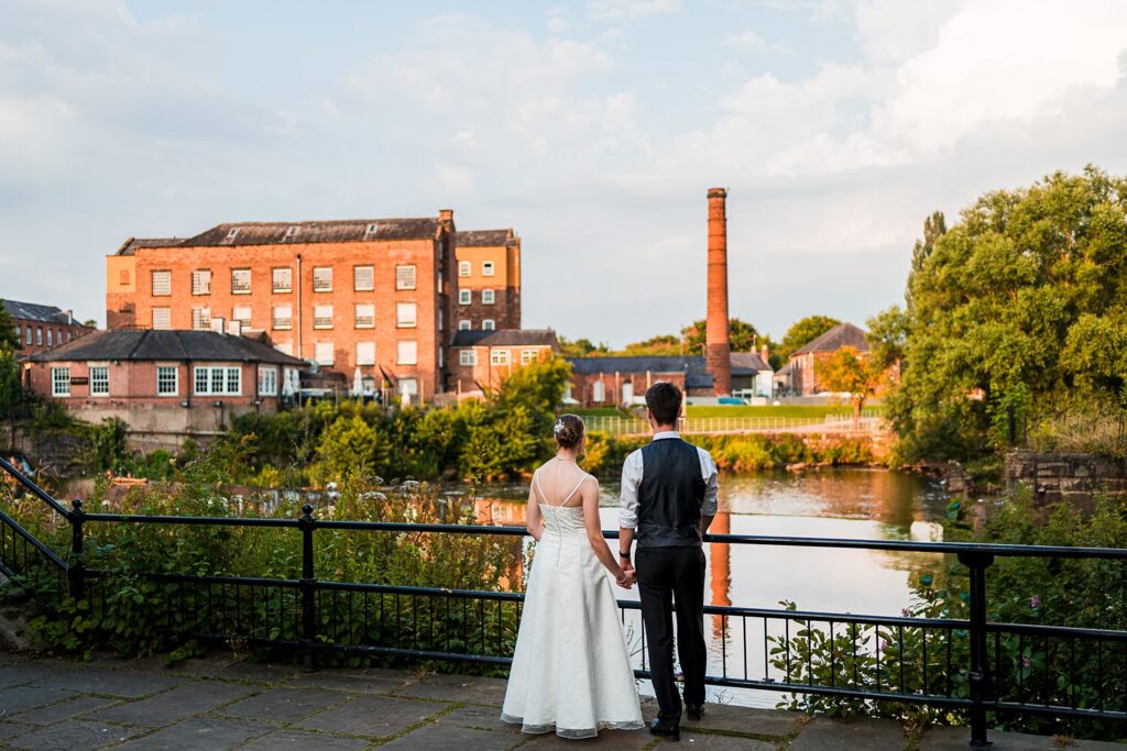 Couple holding hands overlooking river and mill buildings.