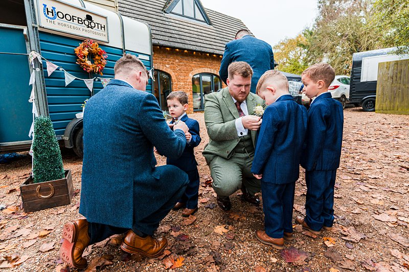 Groomsmen helping boys with boutonnieres outside venue.