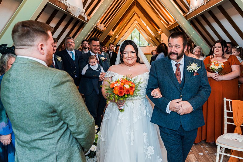 Bride walking down aisle with bouquet and guests.