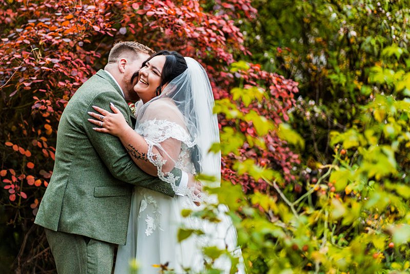 Bride and groom embrace in vibrant garden.