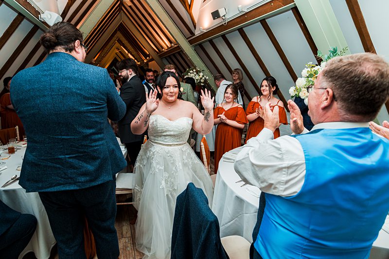 Bride enters reception as guests applaud joyfully.