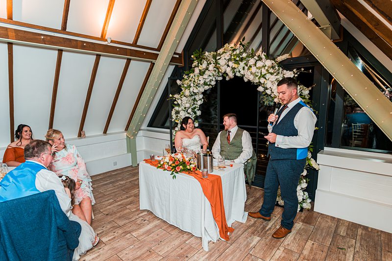 Wedding speech at head table with floral arch.