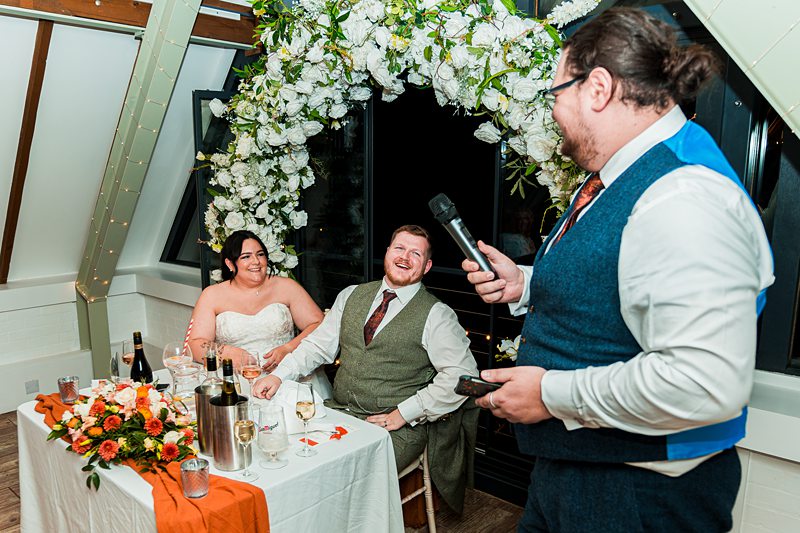 Man giving speech at wedding reception with happy couple.