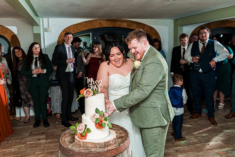 Bride and groom cutting wedding cake surrounded by guests.
