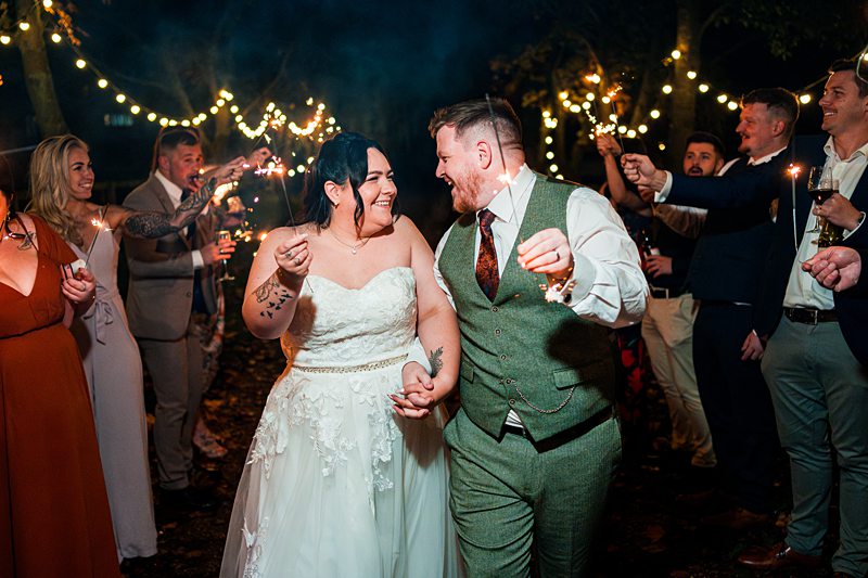 Newlywed couple celebrating with sparklers outdoors.