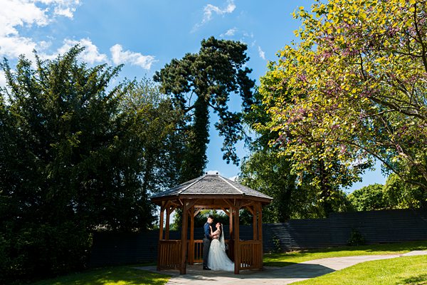 Couple embracing under garden gazebo on sunny day.