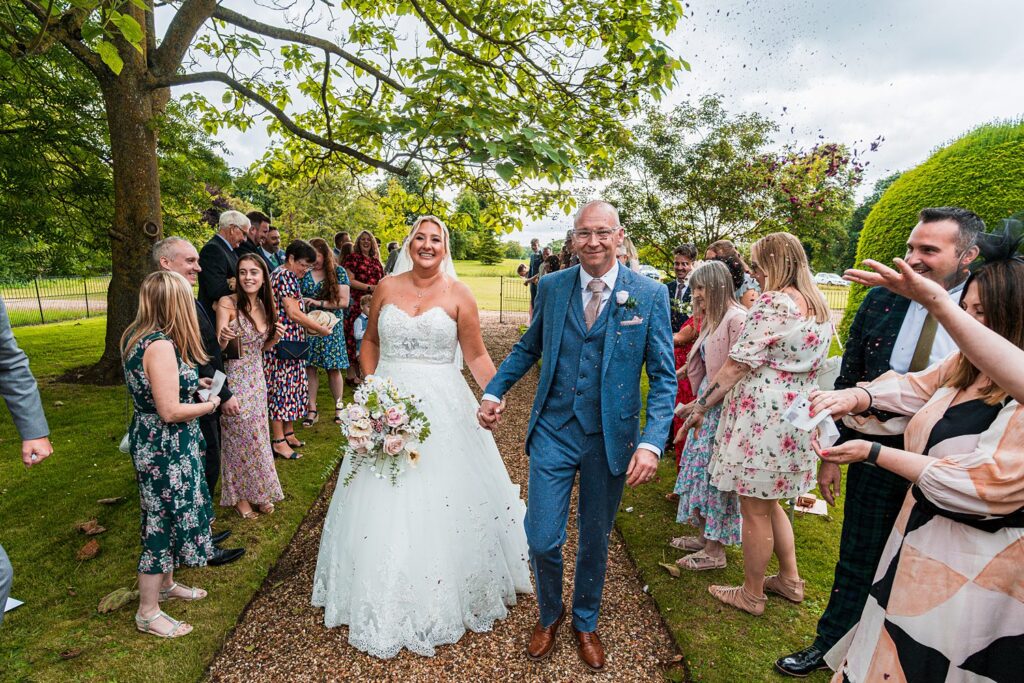 Bride and groom walking through confetti with guests.