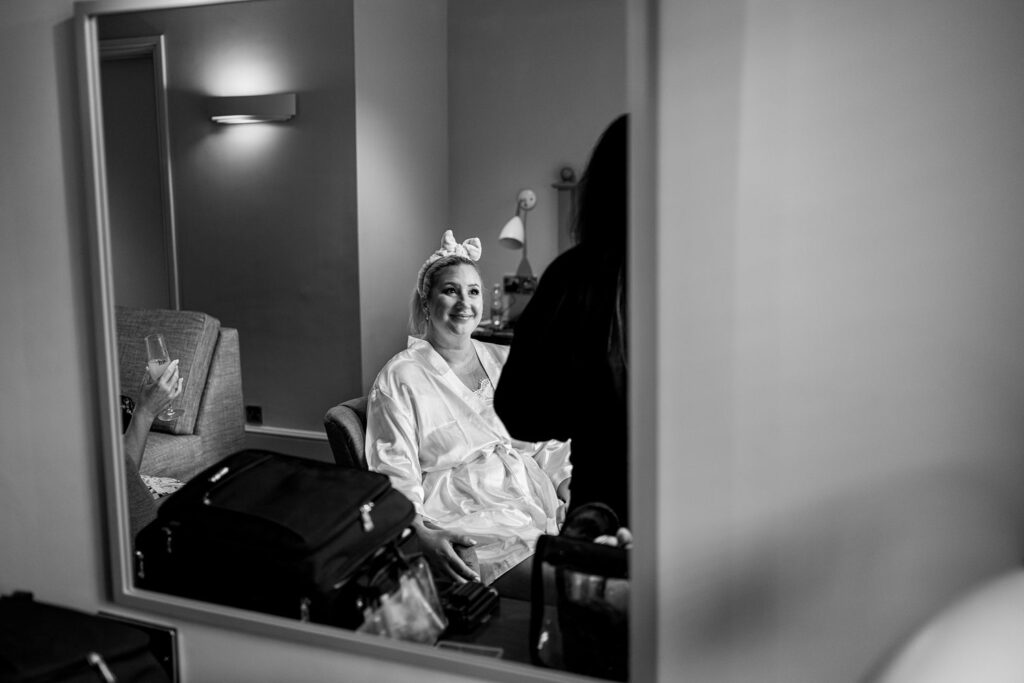 Bride getting ready, smiling in mirror reflection.