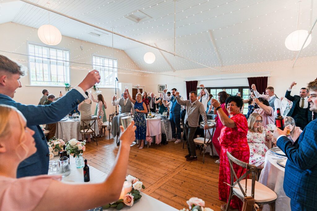 Guests raising glasses at indoor wedding reception.