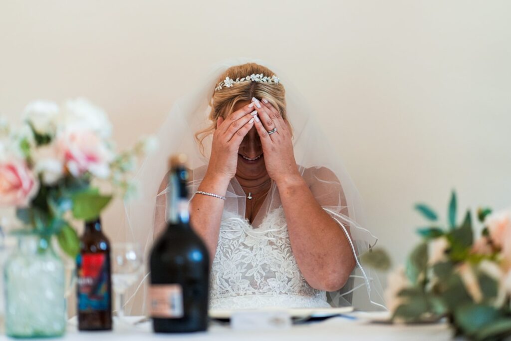 Bride laughing with hands on face at reception.