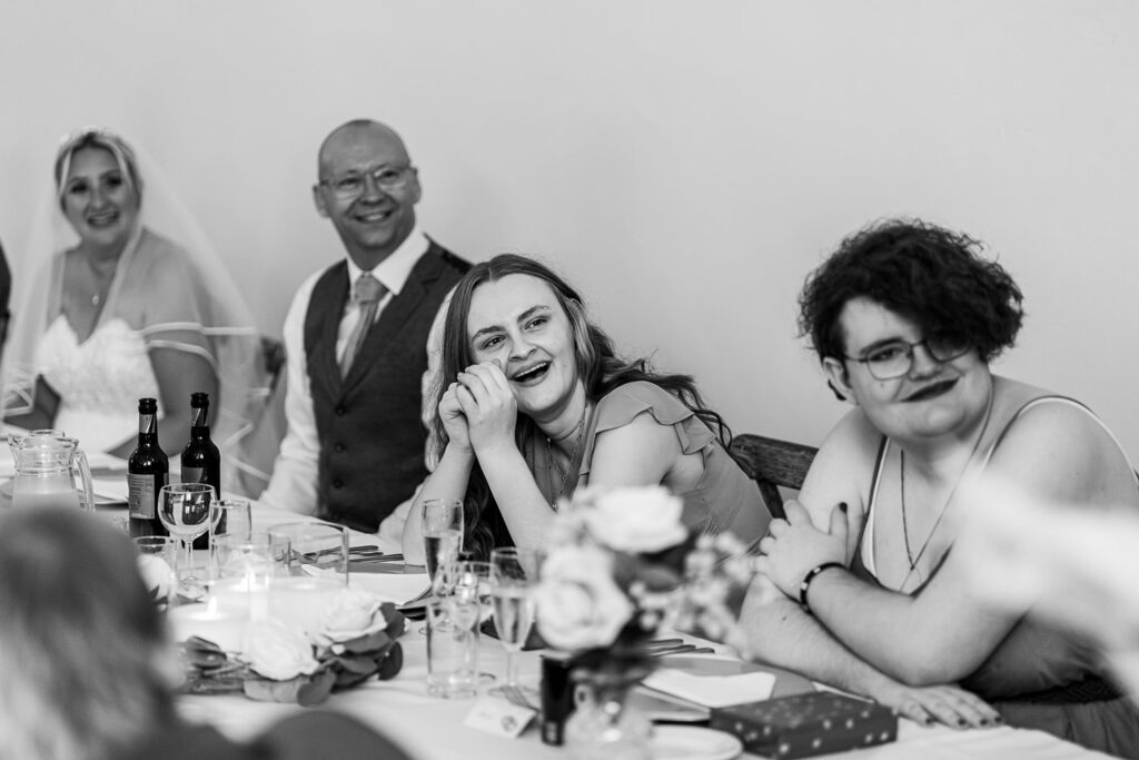 People smiling at wedding reception table.