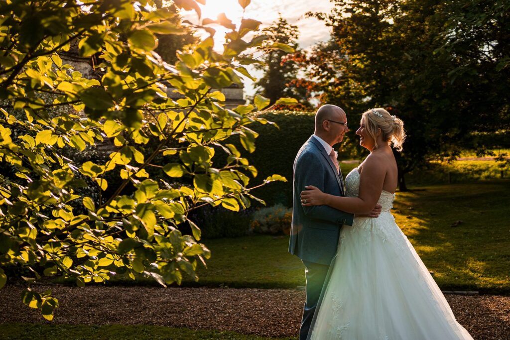 Bride and groom embracing in sunlit garden.
