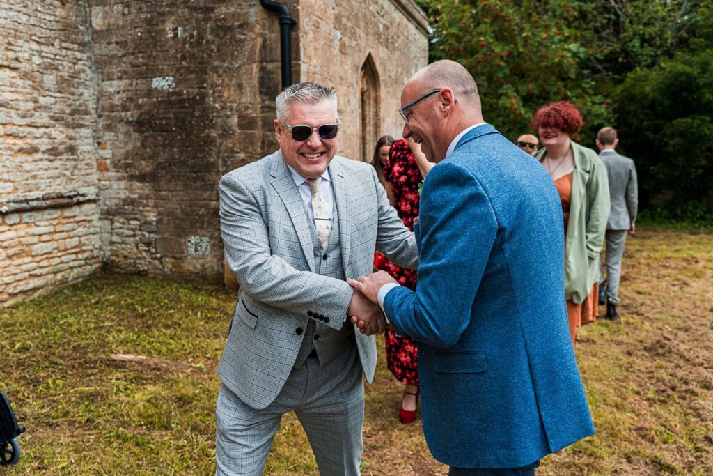 Two men shaking hands at outdoor gathering.