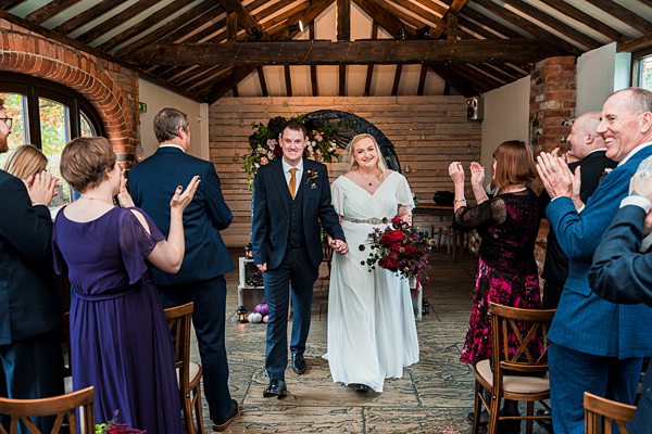 Bride and groom walk down the aisle, guests applauding.