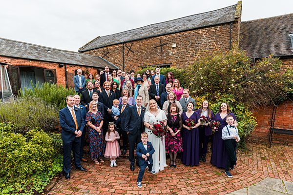 Large wedding group photo outside rustic building.