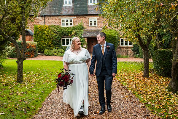 Wedding couple walking in autumn garden path.