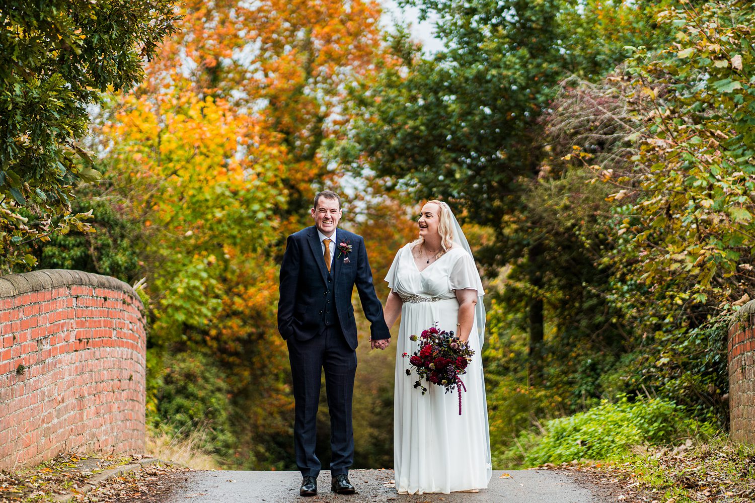 Bride and groom on autumnal bridge.