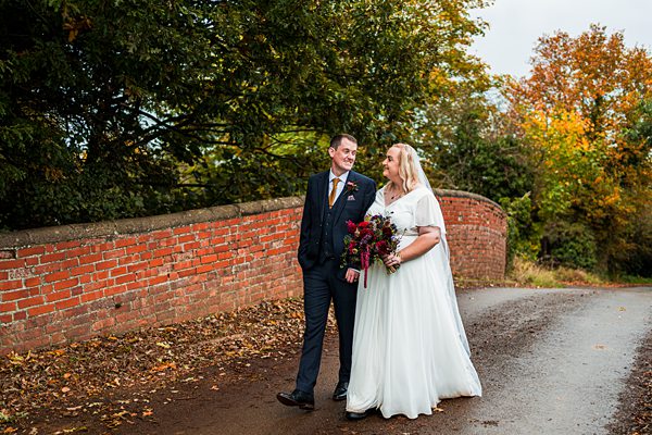 Bride and groom walking on autumnal country lane.
