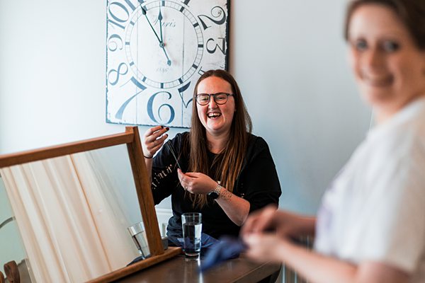 Two women laughing near a mirror and clock.