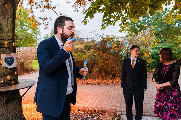 Man blowing bubbles at outdoor gathering.