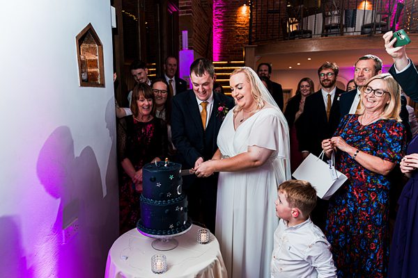 Couple cutting wedding cake surrounded by guests.