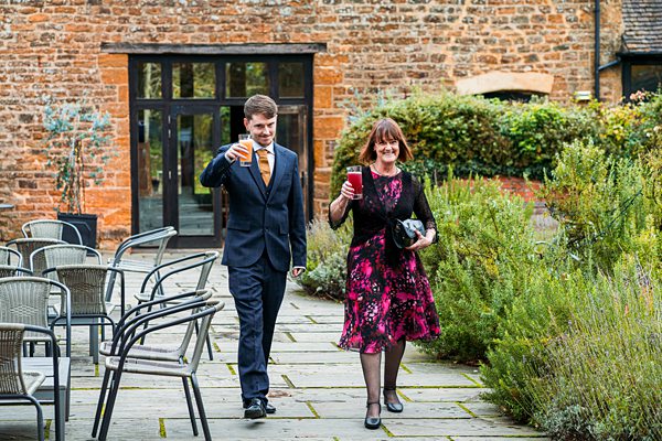 Couple walking outside holding drinks, wearing formal attire.