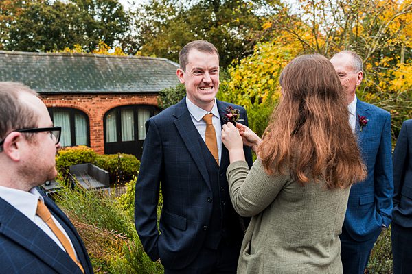Woman adjusts man's boutonniere at outdoor gathering.