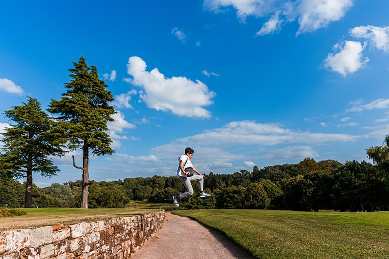 Person jumping on path in scenic parkland.