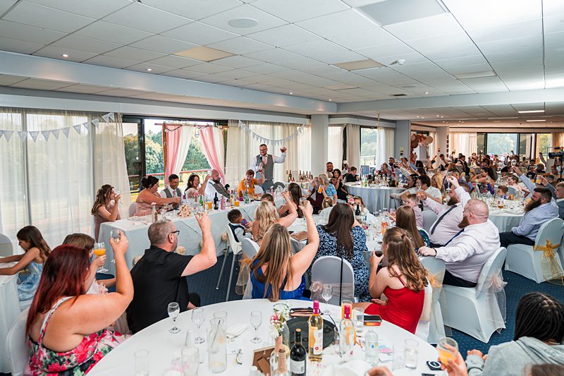 People toasting at a large indoor wedding reception.